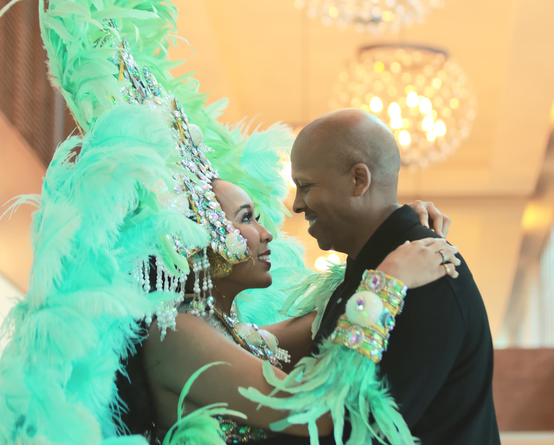 Breanna in a green feathered carnival costume, dancing close with Rob