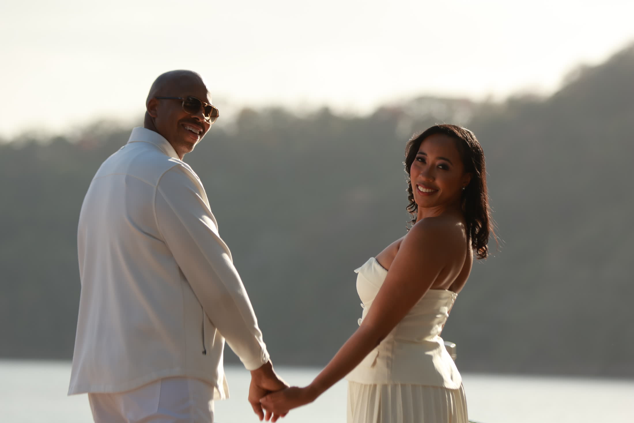 Breanna and Rob holding hands by the water, looking back and smiling